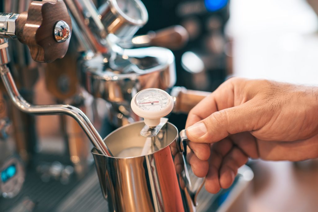 Barista is using temperature tool to prepare milk in milk frother.